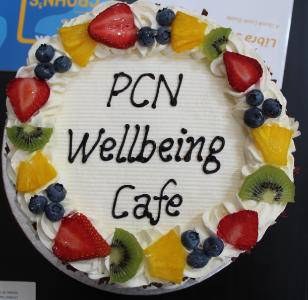 A cake with PCN Wellbeing Cafe written in icing